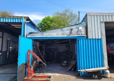 Front view of the garage during demolition, showing blue doors and construction equipment.