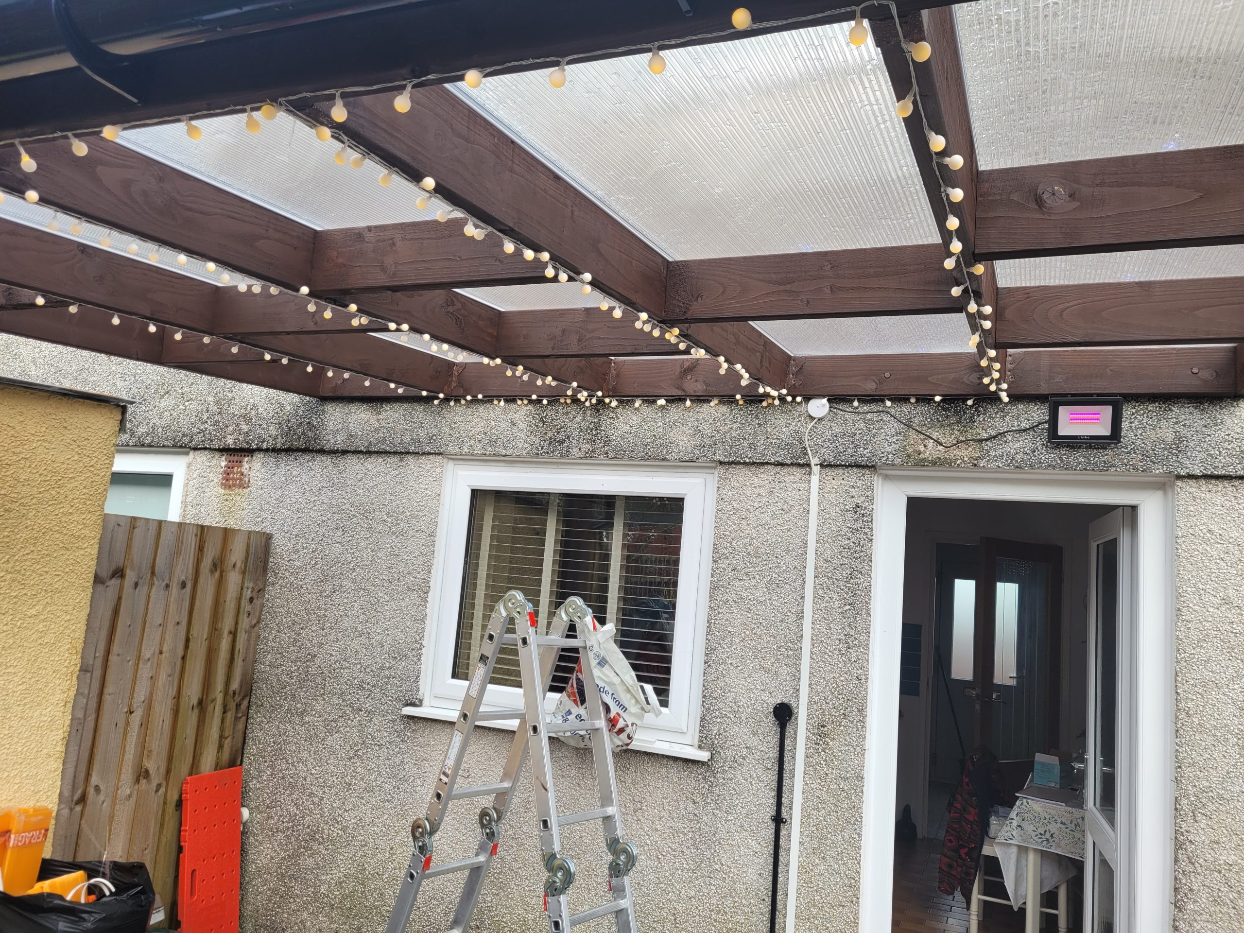 Pergola with Integrated Lighting Pergola with clear roof panels and decorative string lighting installed over garden patio